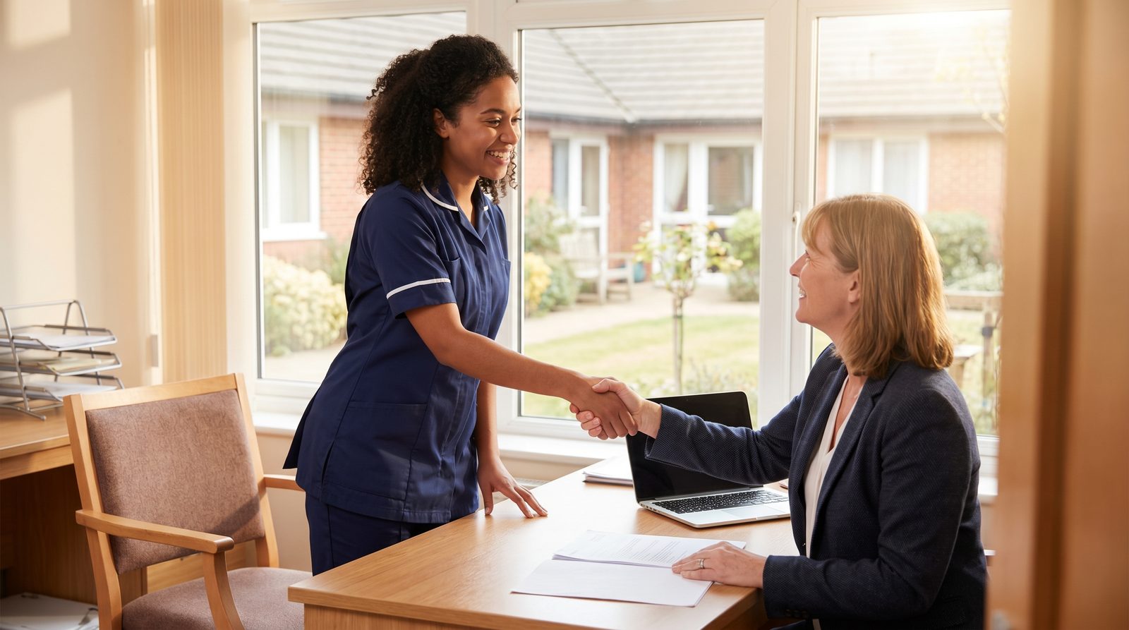 Confident PSW job candidate in professional attire shaking hands with a hiring manager at the start of a personal support worker job interview in a care facility office